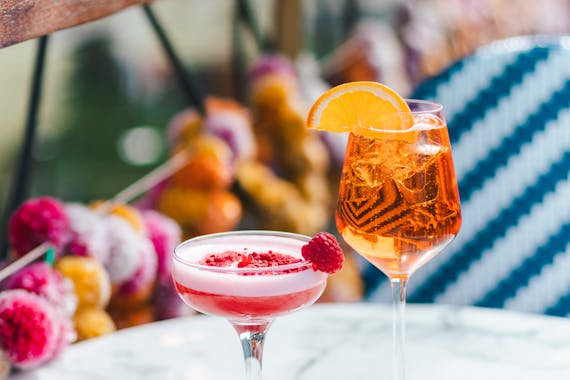Two colourful cocktails; one is pink and in a martini glass and the other is orange and in a large glass.