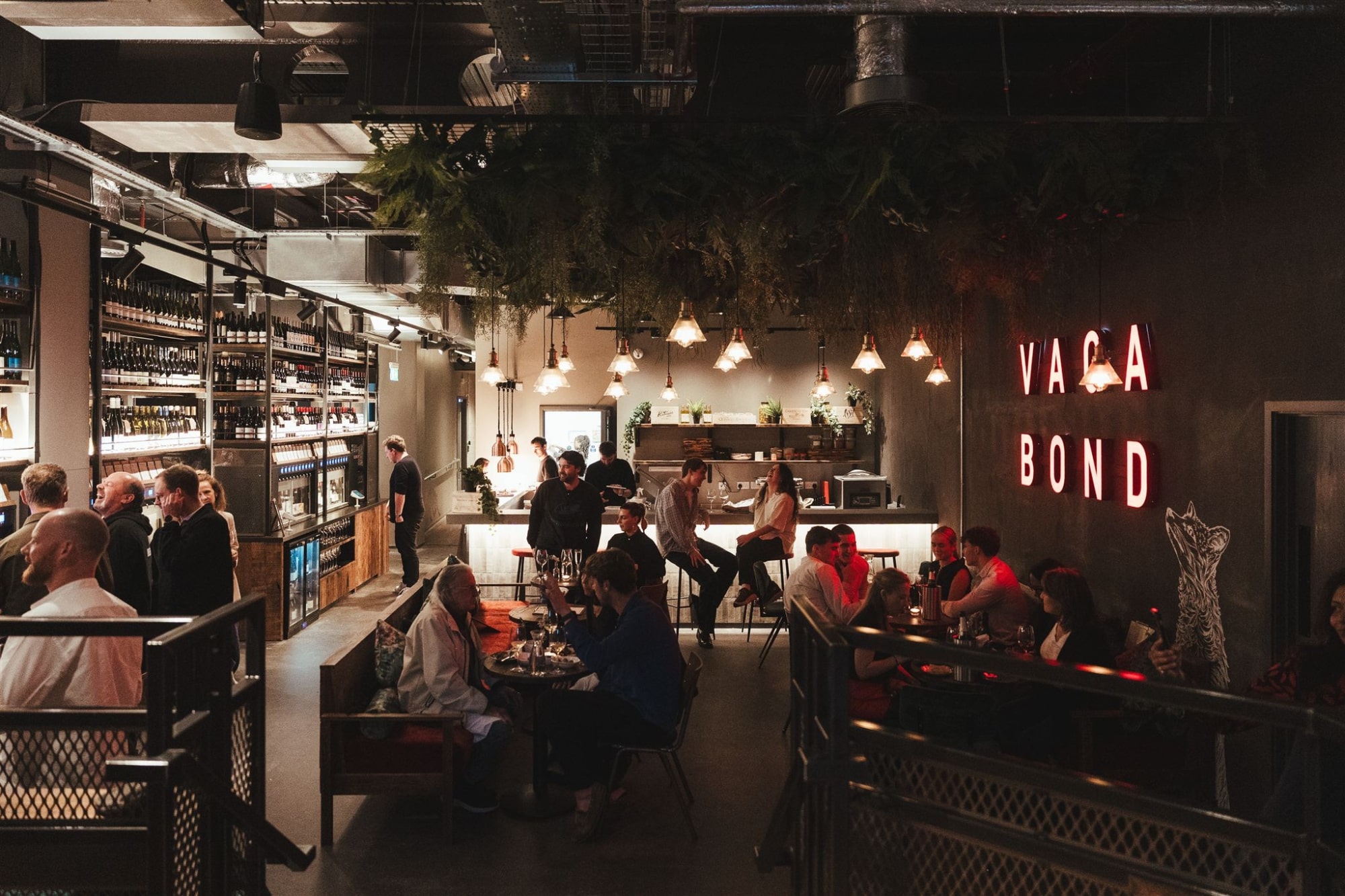 The image captures the interior of a stylish and contemporary bar or wine merchant, characterized by a blend of industrial and cozy design elements.