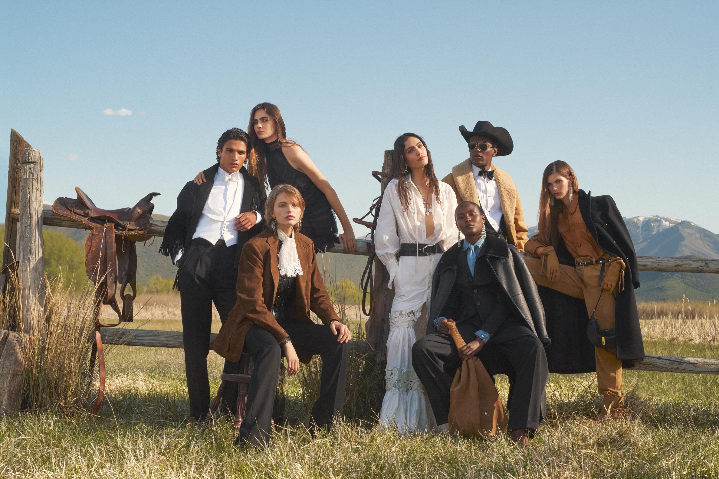 The photo features a group of seven models posing outdoors in what appears to be a Western or ranch setting, possibly in the mountains, given the background. They are dressed in a mix of elegant, rugged, and Western-inspired clothing, which is a signature style for the brand.