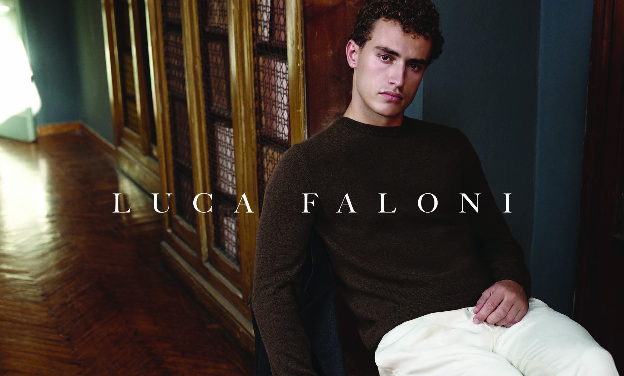 The image is an advertisement featuring a man wearing a dark brown, long-sleeved sweater and light-colored trousers.