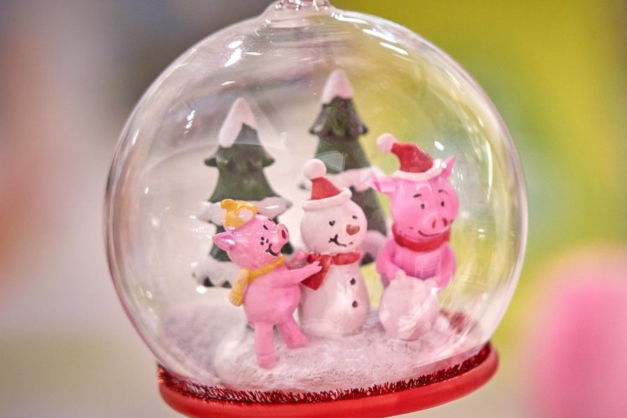 This is a close-up, shallow depth-of-field photograph of a Christmas ornament. The ornament is a clear glass globe (similar to a snow globe, but hanging) with a red ring around its base and a red ribbon attached for hanging.