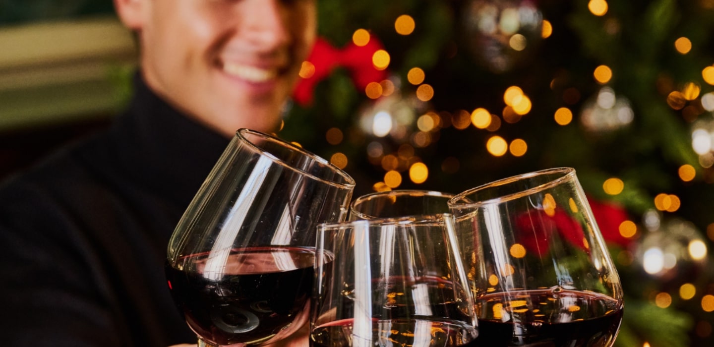 Wine glasses clinking together with christmas tree in background