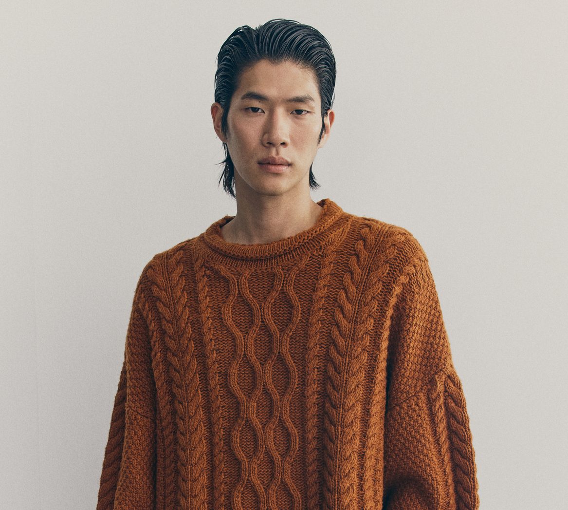 A model wears a burnt orange cable knit jumper.