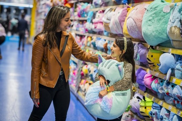 A mum and daughter shop together in Smyth's toy shop. The daughter hugs a squishmallow.