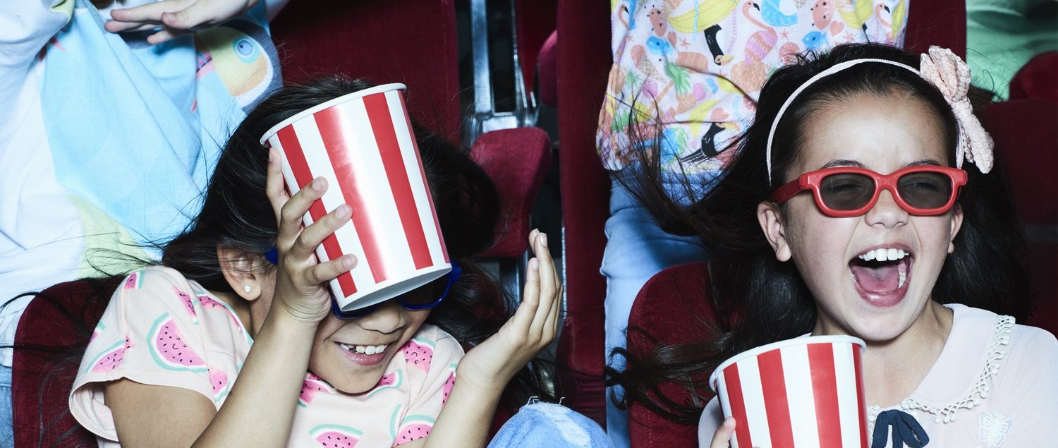 Two young people excitedly watch a film with popcorn.