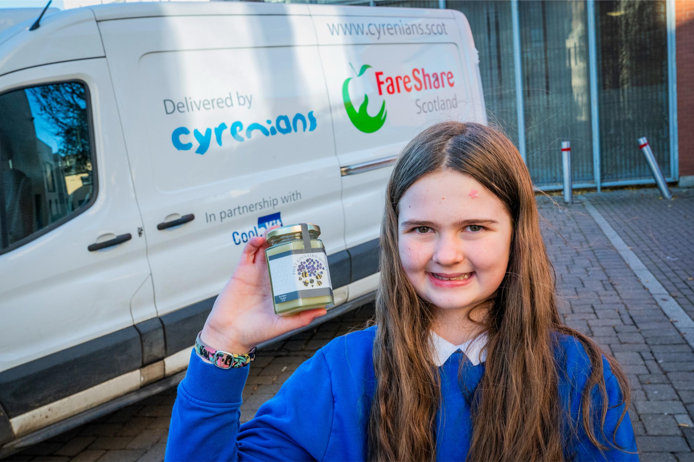Young schoolgirl smiling holding a jar of honey