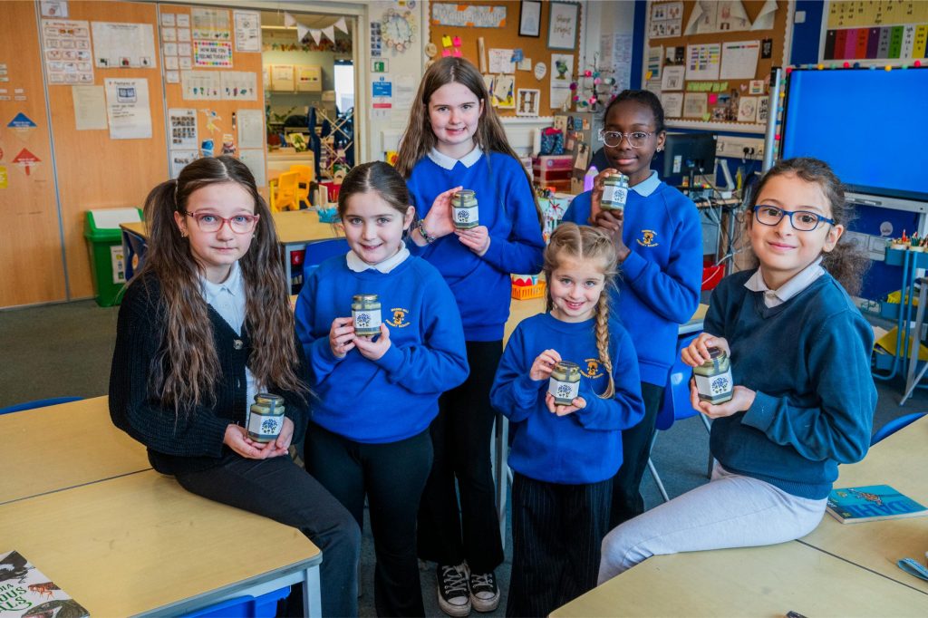 Group of school children with their teacher holding jars of honey