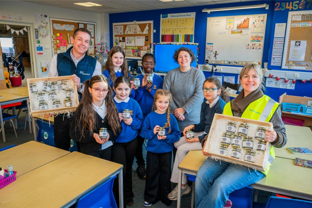 Group of school children with their teacher holding jars of honey