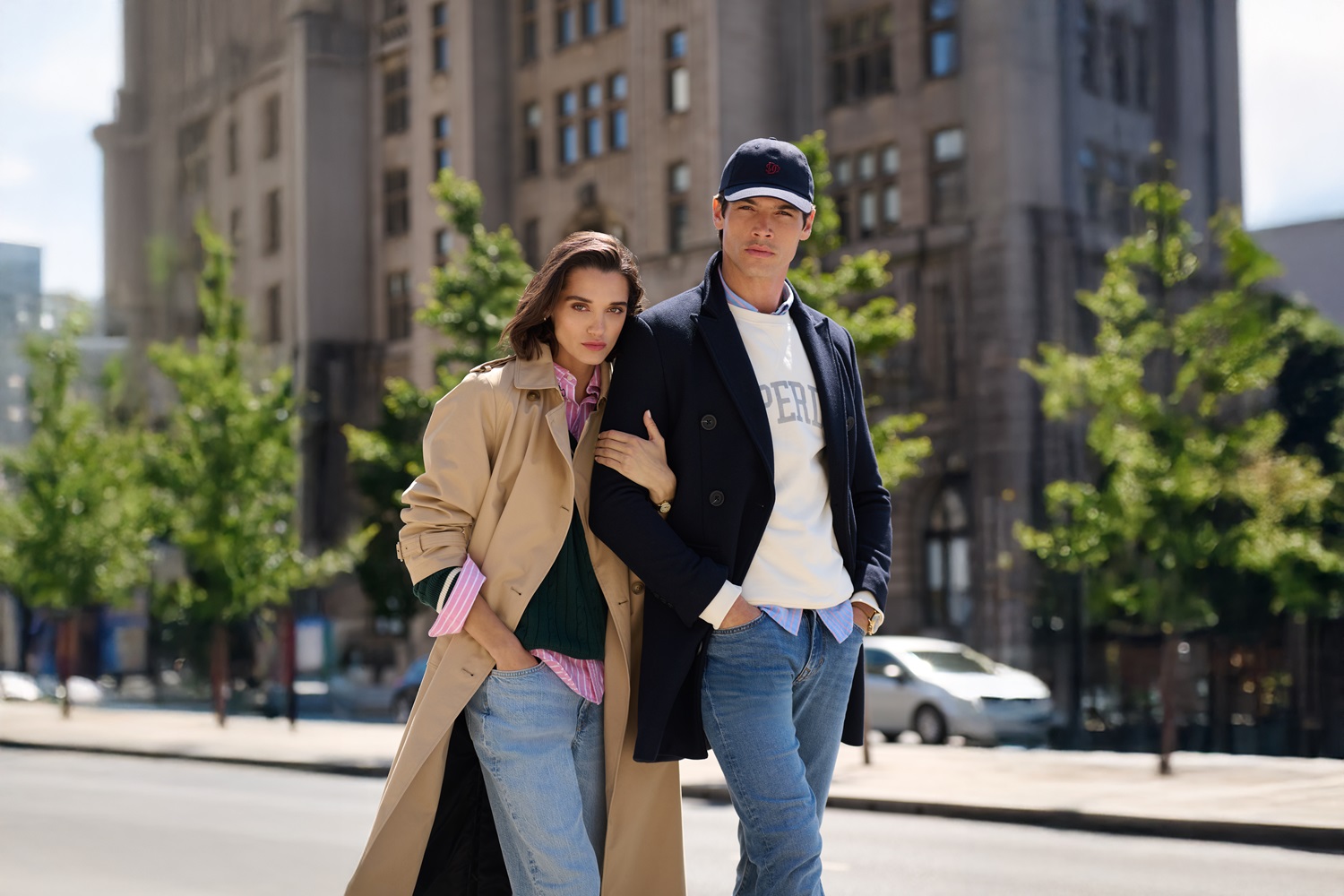 A man and woman stand together on a roadside wearing Superdry clothes including a trench coat/jacket