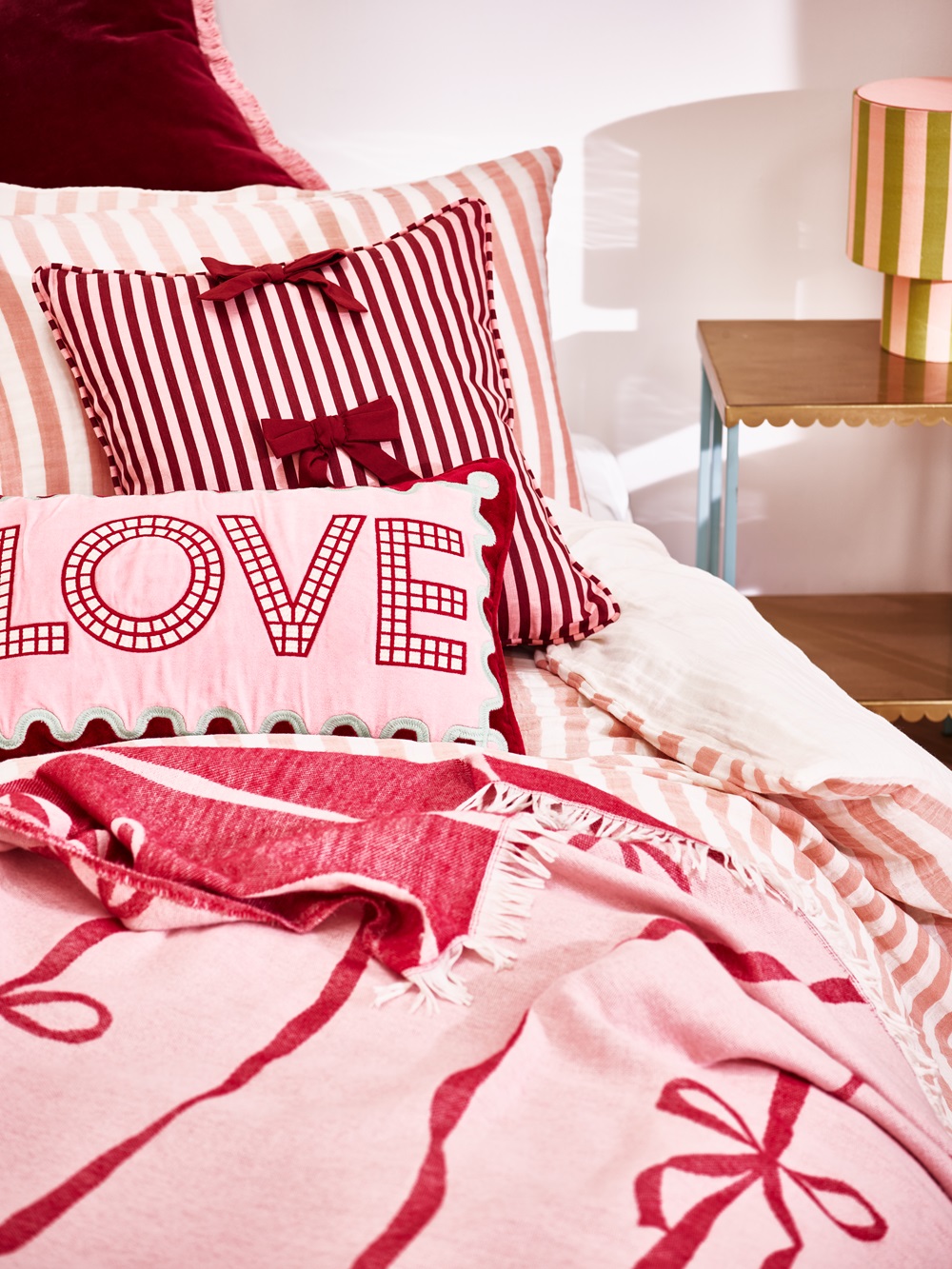 Some pink bedding on a bed with bow patterns and the word love on them.