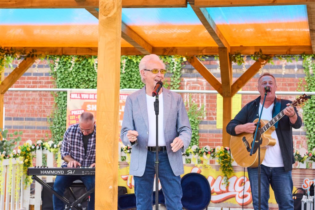 Elderly man with blue jacket on singing on stage with a band