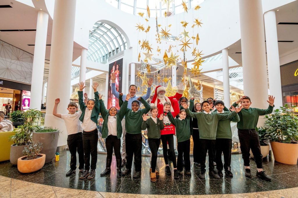 A group of children raise their hands above their heads with the centre director and santa claus in Meadowhall.