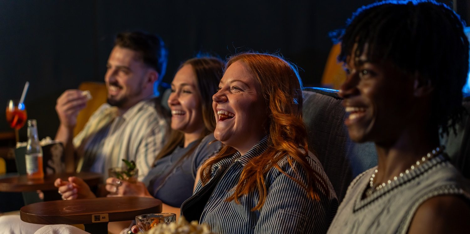 Friends sit and smile watching a film in the cinema