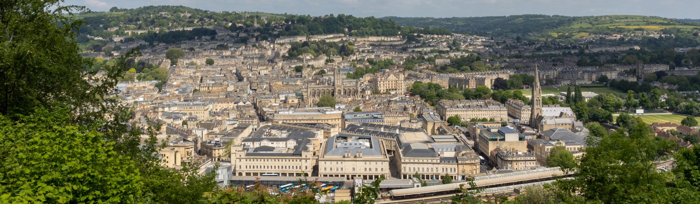 The image is a wide, panoramic view of the city of Bath, England, likely taken from a hillside overlooking the centre.