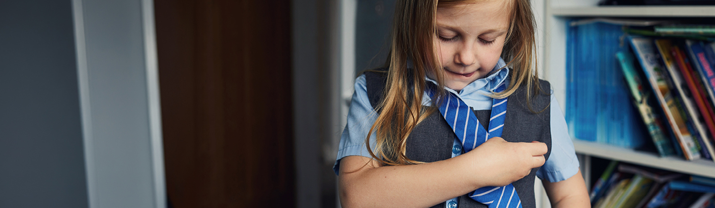Young girl putting on her school uniform tie
