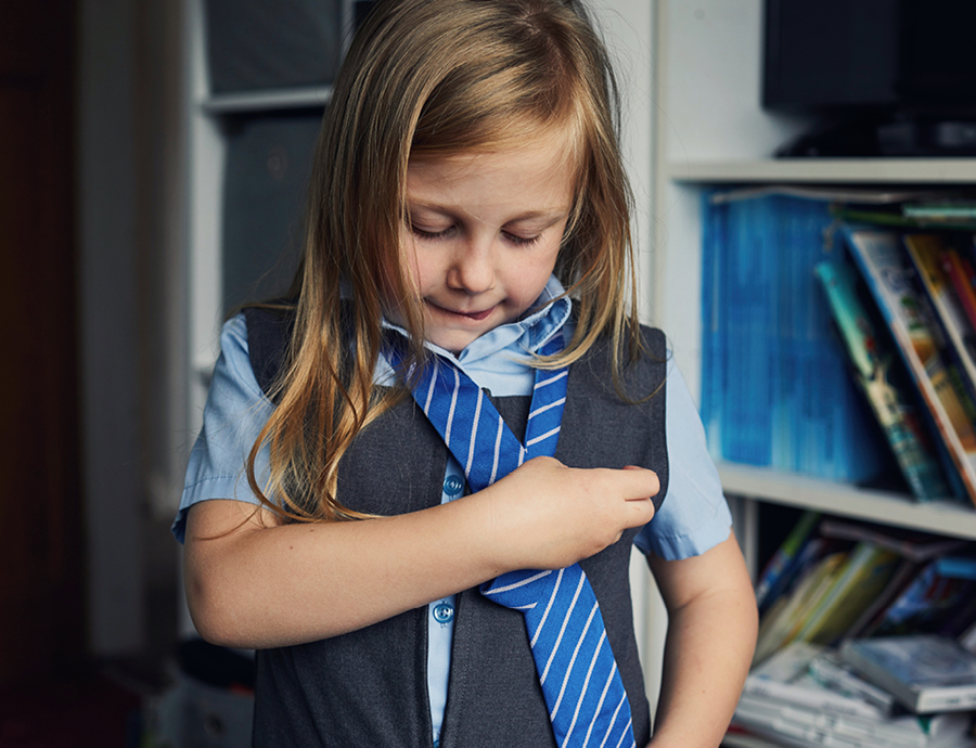 Young girl putting on her school uniform tie
